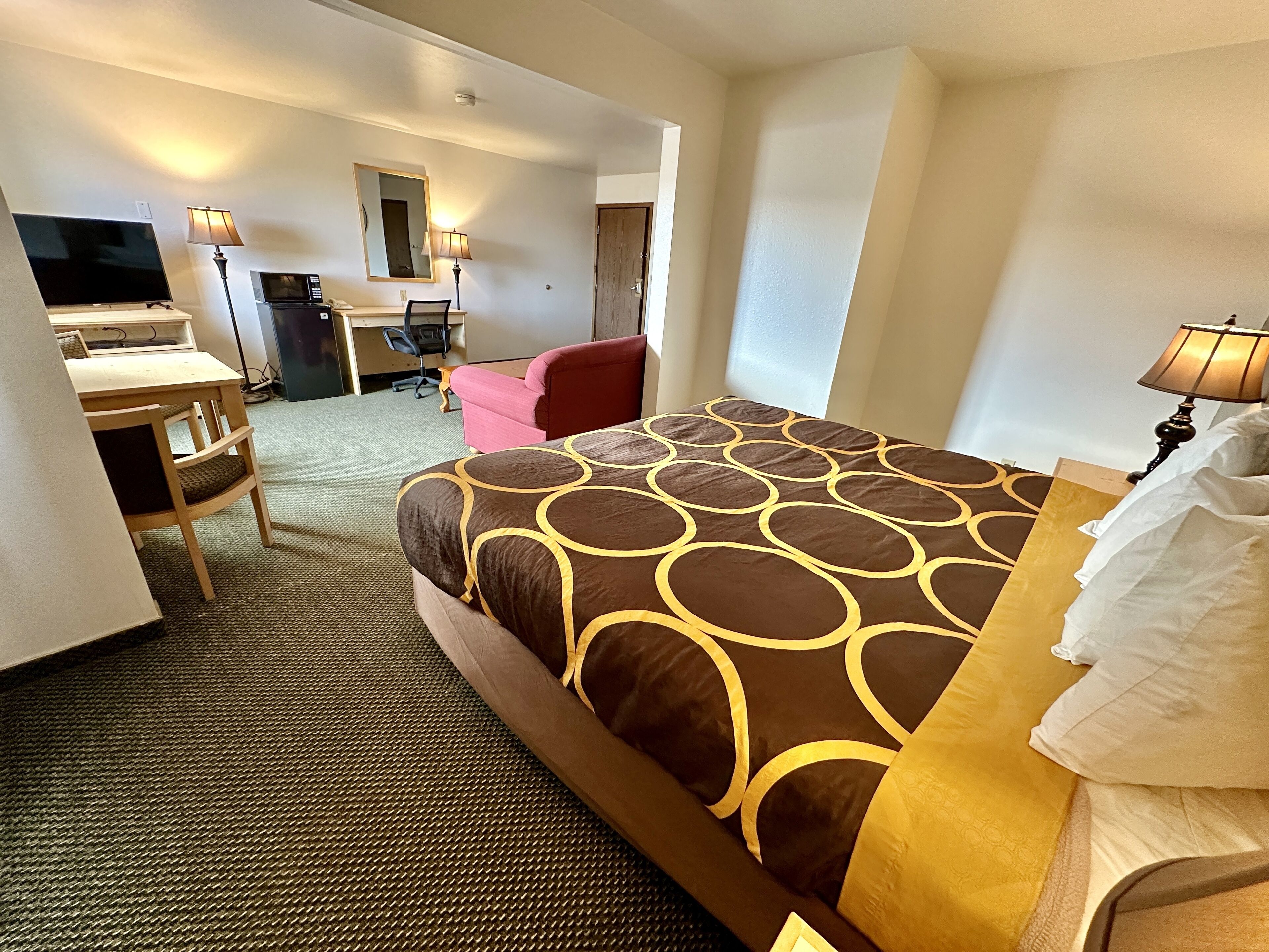 A hotel room with a bed, a desk, a chair, a TV, and a mirror.