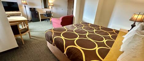Une chambre d’hôtel avec un lit, un bureau, une chaise, une télévision et un miroir.