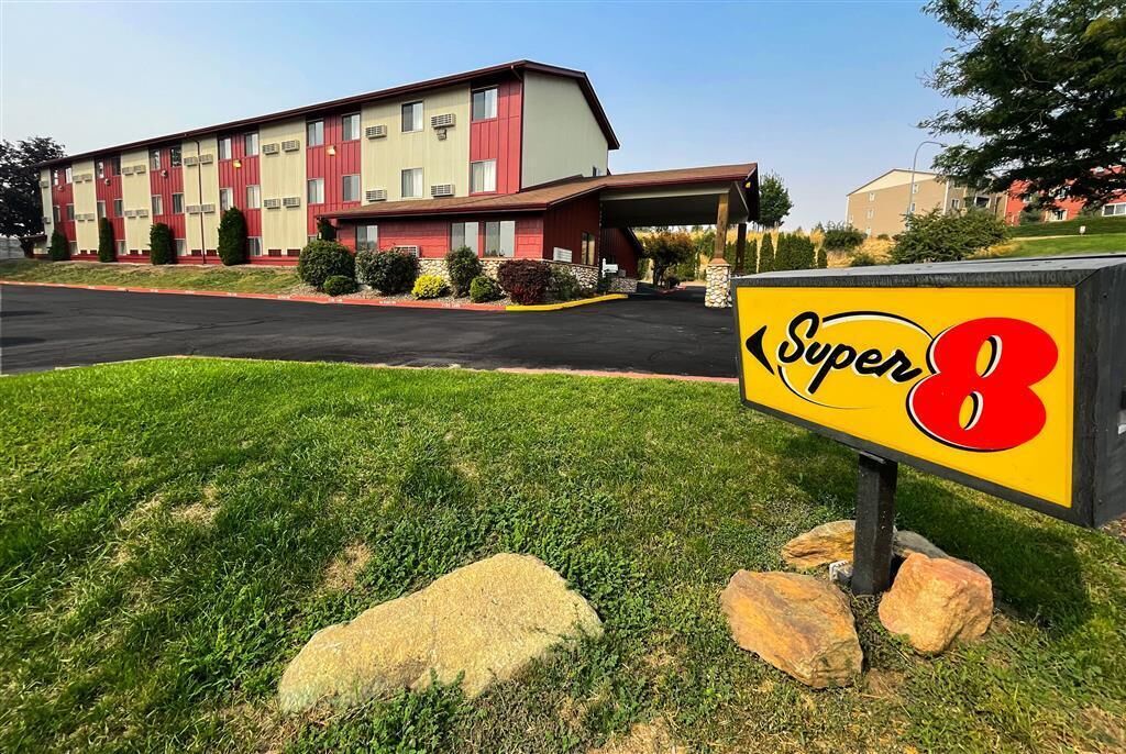Ein Motel mit rotem und beigem Äußeren, einem überdachten Parkbereich und einem Schild mit der Aufschrift 'Super 8'.