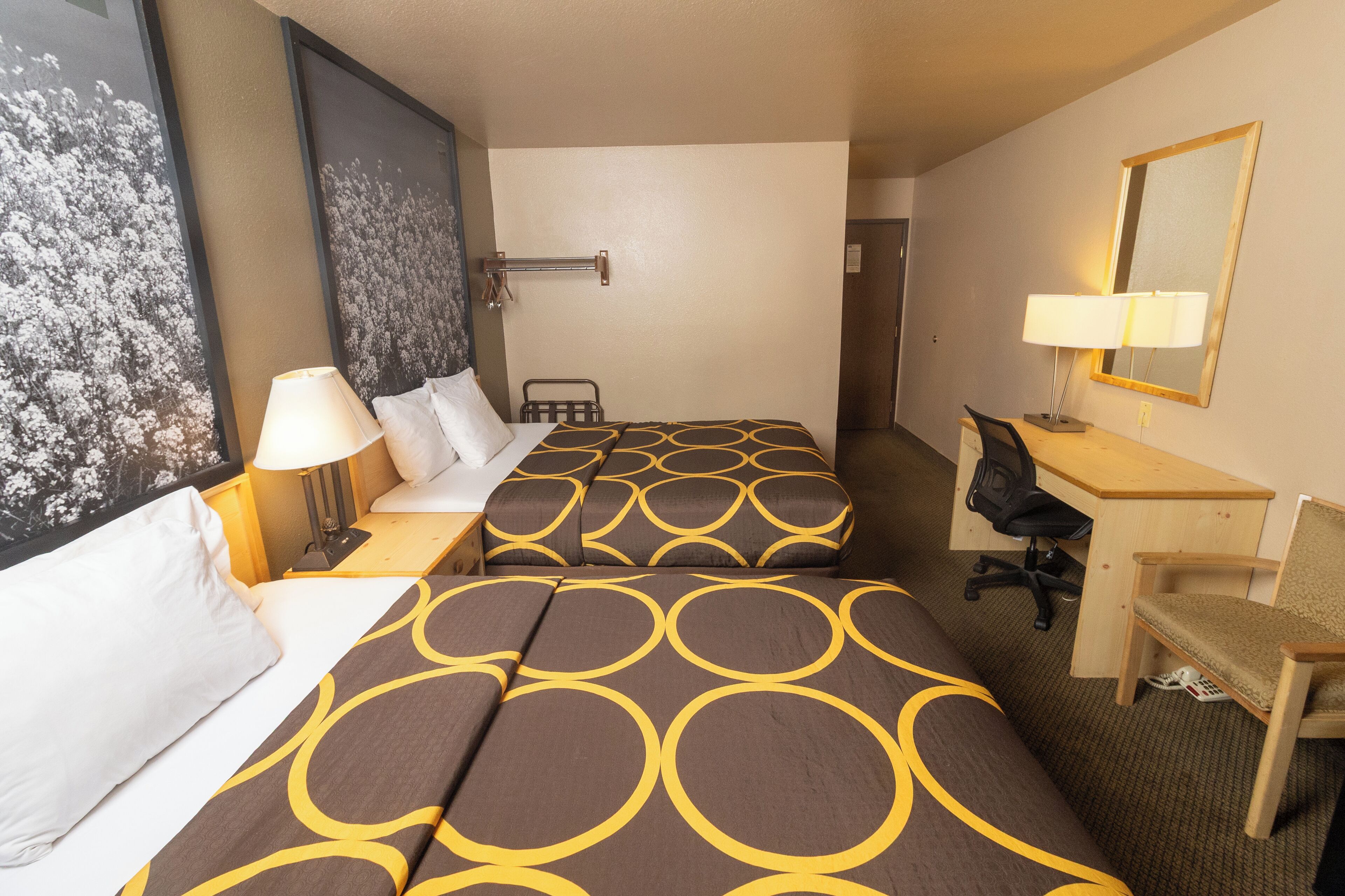 A hotel room with two beds, a desk, a chair, a lamp, and a large framed picture on the wall.