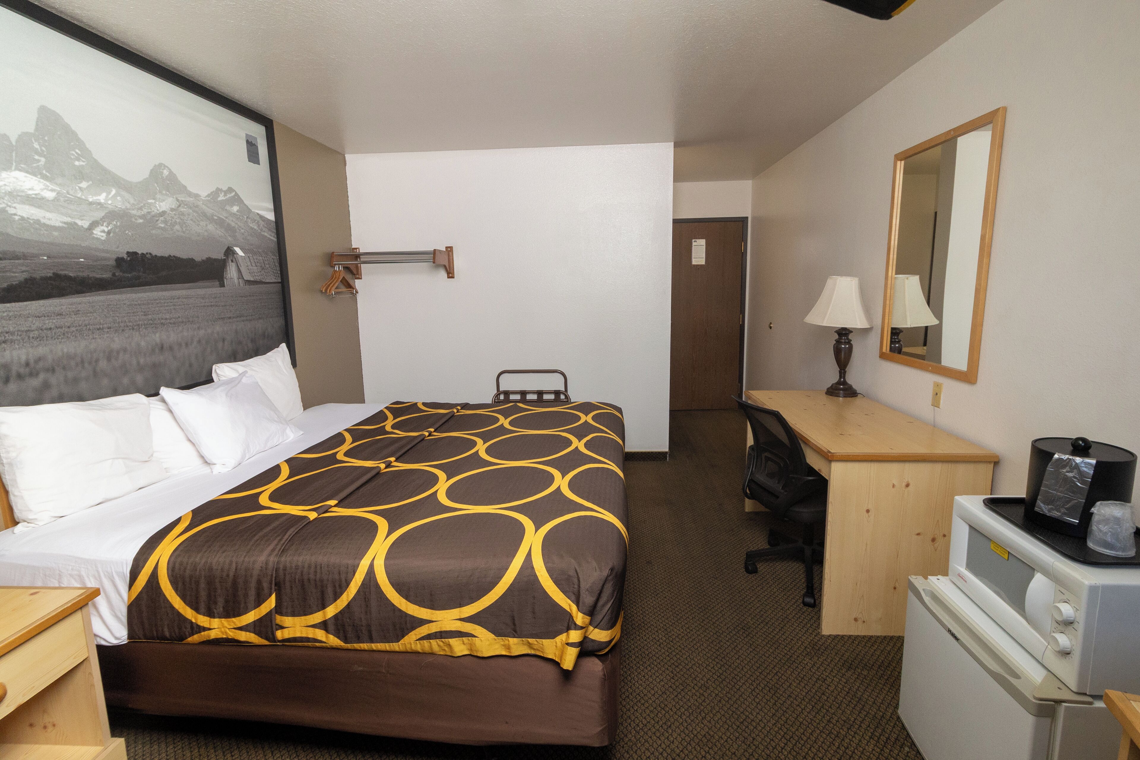 A hotel room with a bed, desk, chair, and a small kitchenette.