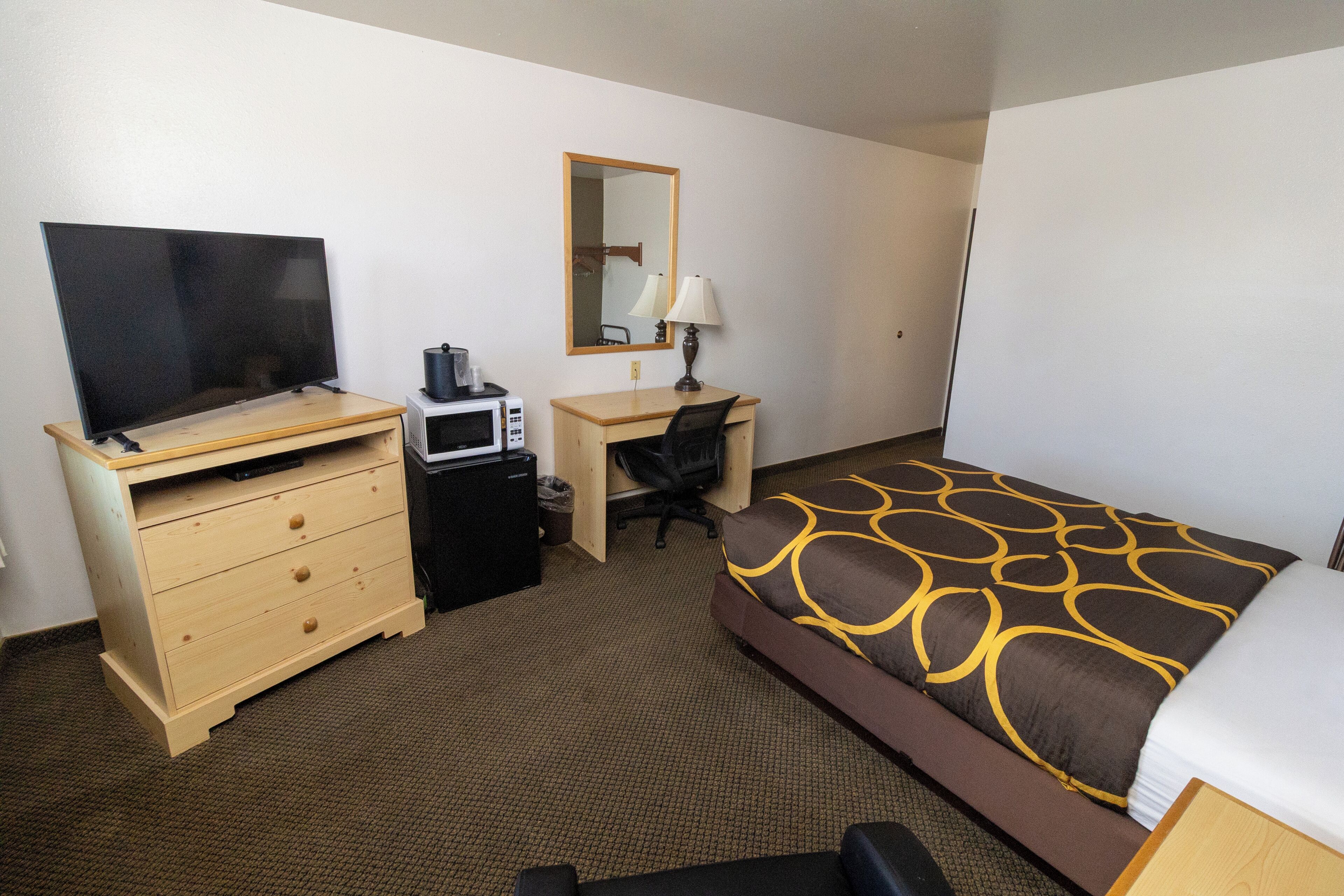 A hotel room with a bed, a desk, a television, a microwave, and a chair.