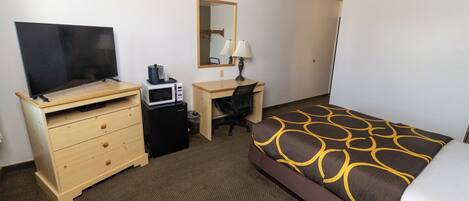 A hotel room with a bed, a desk, a television, a microwave, and a chair.
