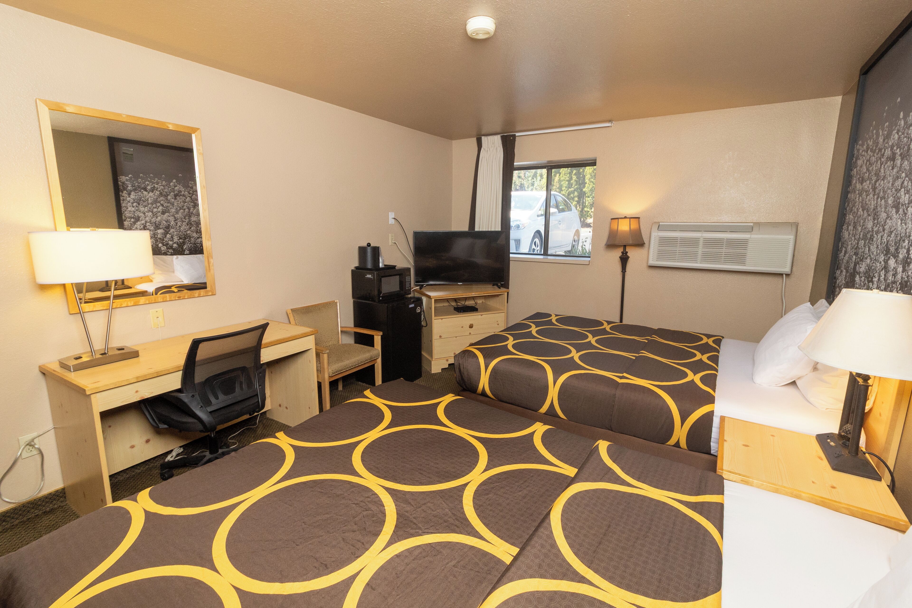 Habitación de hotel con dos camas, un escritorio, una silla, un televisor y una ventana con vista a un coche.