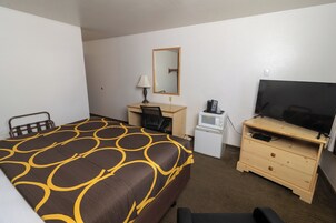 Habitación de hotel con cama, escritorio, silla, televisor, microondas y cómoda.