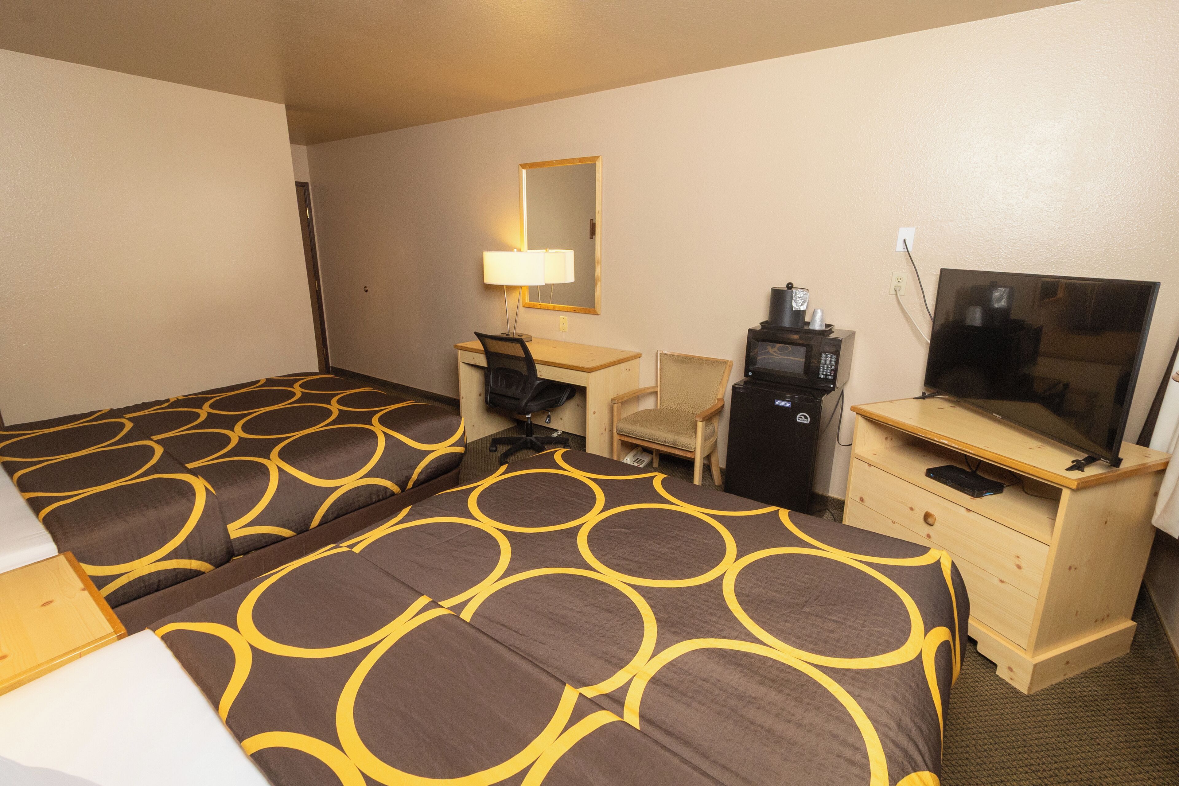 Habitación de hotel con dos camas, un escritorio, una silla, un televisor y un espejo.