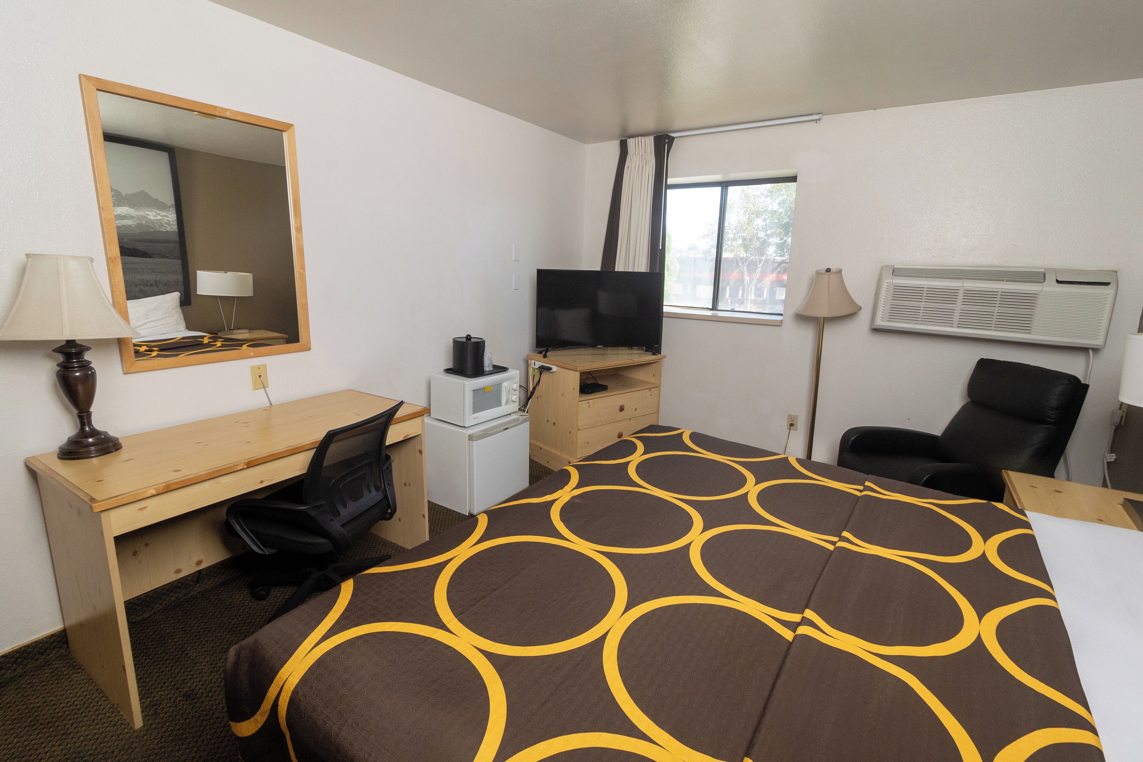 Une chambre d’hôtel avec un lit, un bureau, une chaise, une télévision et une fenêtre avec des rideaux.
