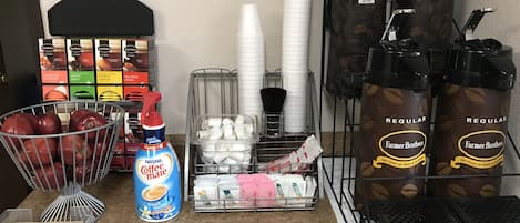 A coffee station with coffee makers, disposable cups, and a basket of apples.