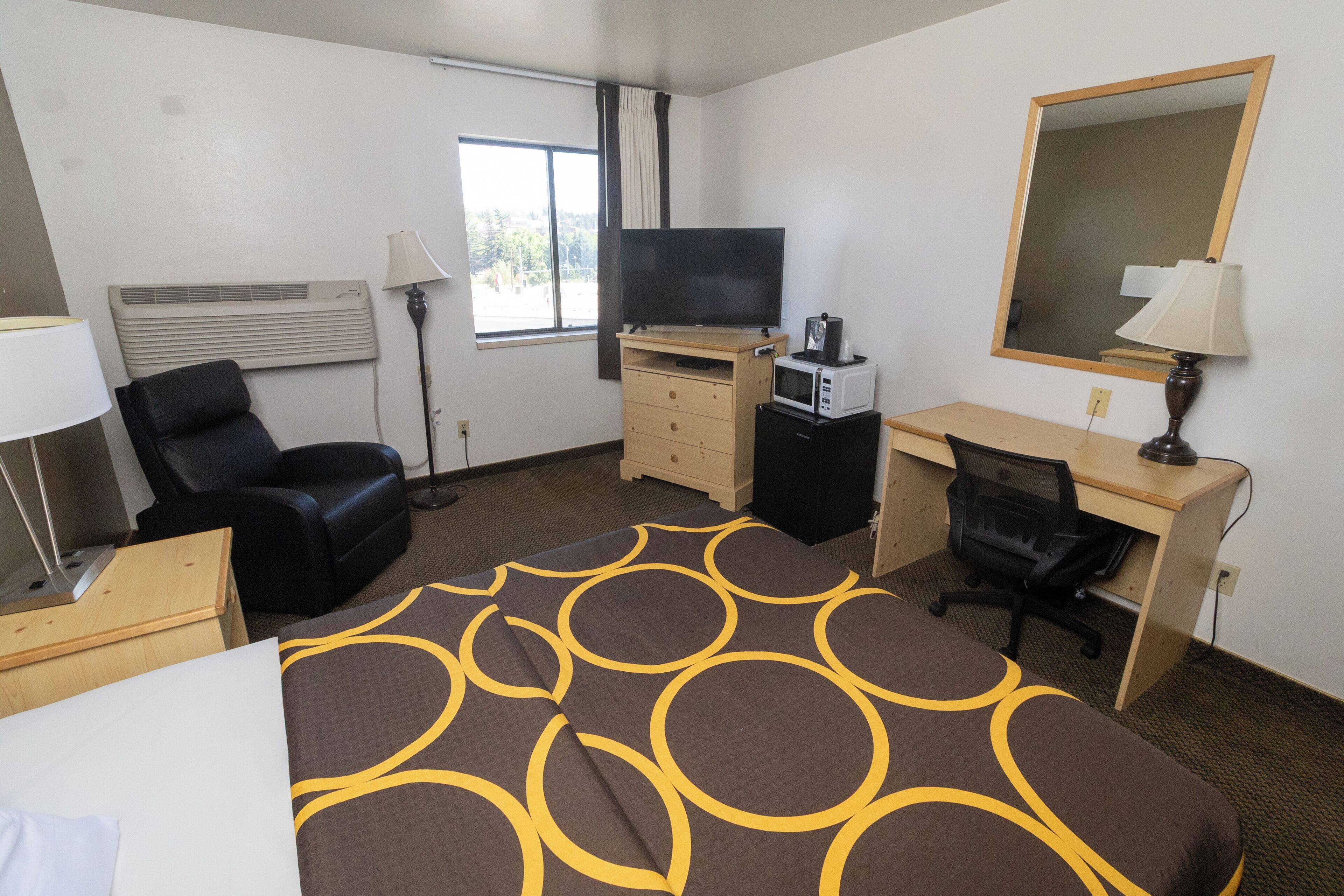 A hotel room with a bed, a desk, a chair, a TV, a microwave, and a mirror.