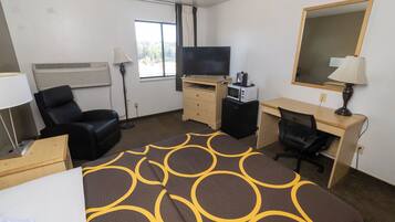 A hotel room with a bed, a desk, a chair, a TV, a microwave, and a mirror.