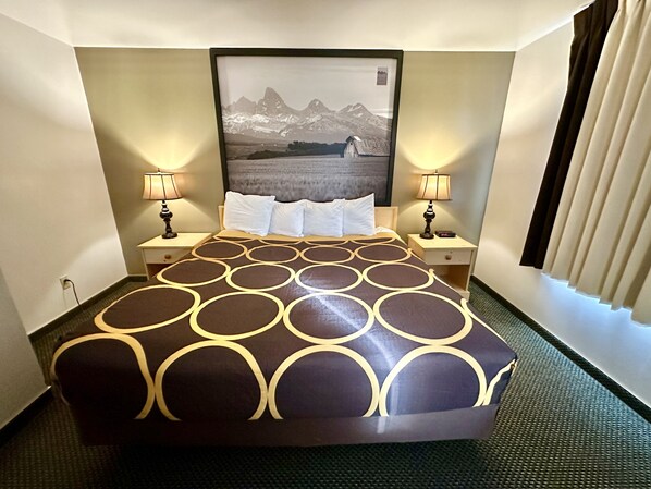 A hotel room with a large bed, two bedside tables, a headboard with a framed picture, and two lamps.