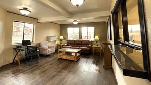 A living room with a brown leather sofa, a wooden coffee table, a patterned armchair, a desk with a computer, and two lamps. - FairBridge Inn & Suites Moscow/Pullman (Moscow)