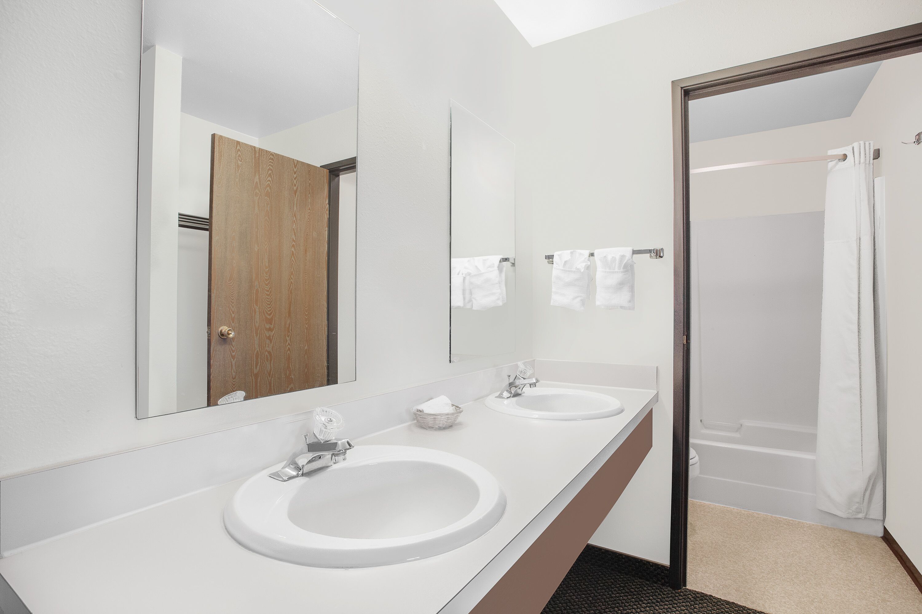 Une salle de bain moderne avec deux lavabos, un grand miroir et une porte de douche en verre.