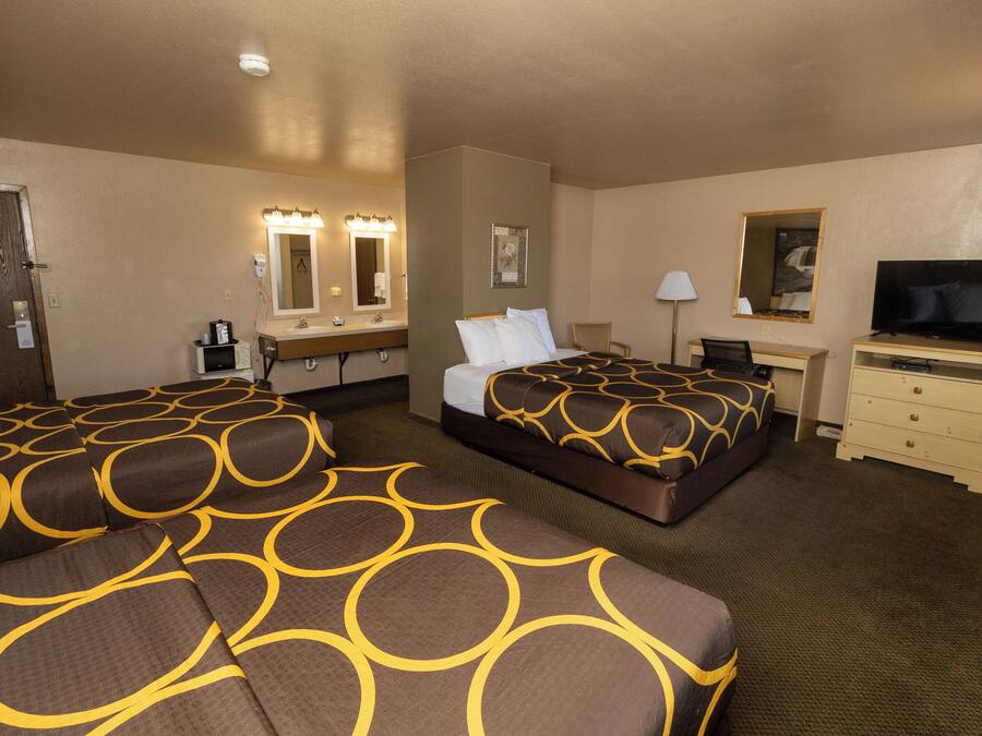 A hotel room with two beds, a desk, a television, and a bathroom with a mirror and lights.