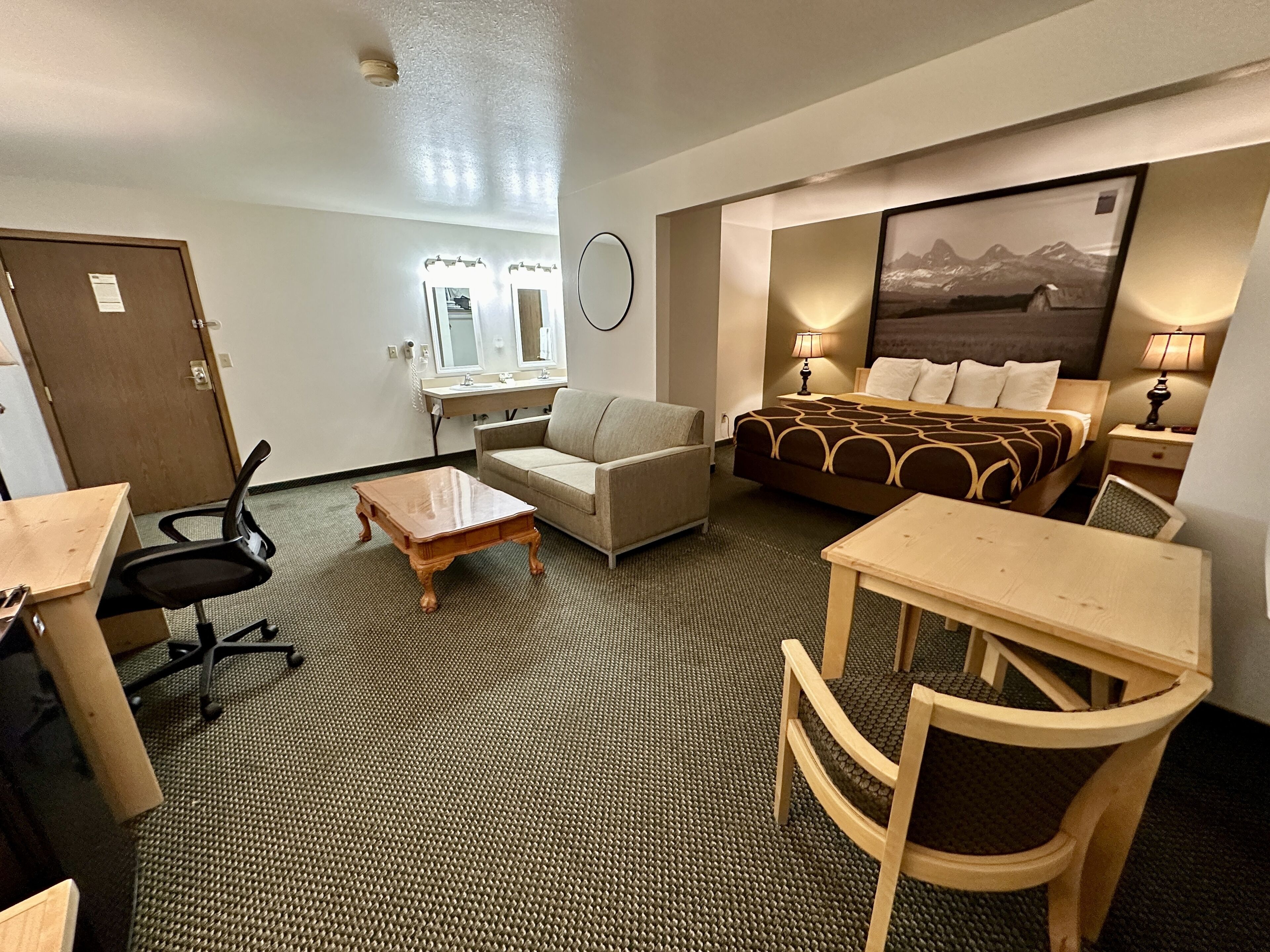 A hotel room with a bed, a sofa, a desk, and a chair. There is a window with a view of mountains.
