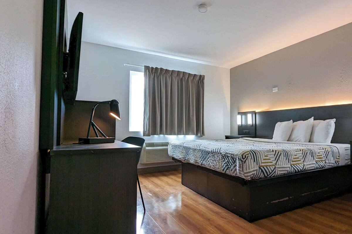 A hotel room with a bed, bedside tables, a desk with a lamp, a TV, and a window with curtains.