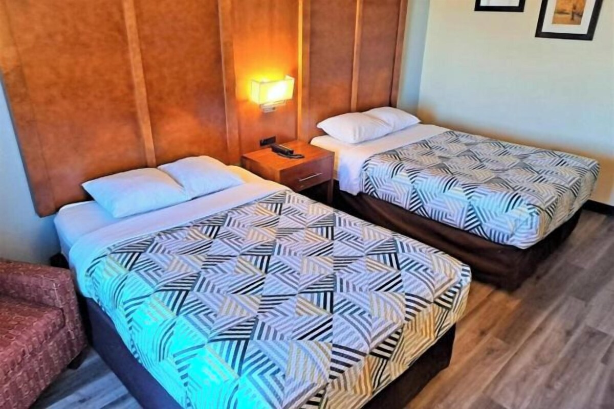 Two twin beds with patterned bedding, a wooden headboard, a nightstand with a phone, and a wall-mounted lamp.