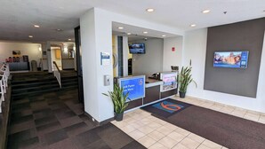 A reception area with a counter, a television mounted on the wall, and a staircase leading to another floor. - Motel 6 Framingham, MA - Boston West (Framingham)