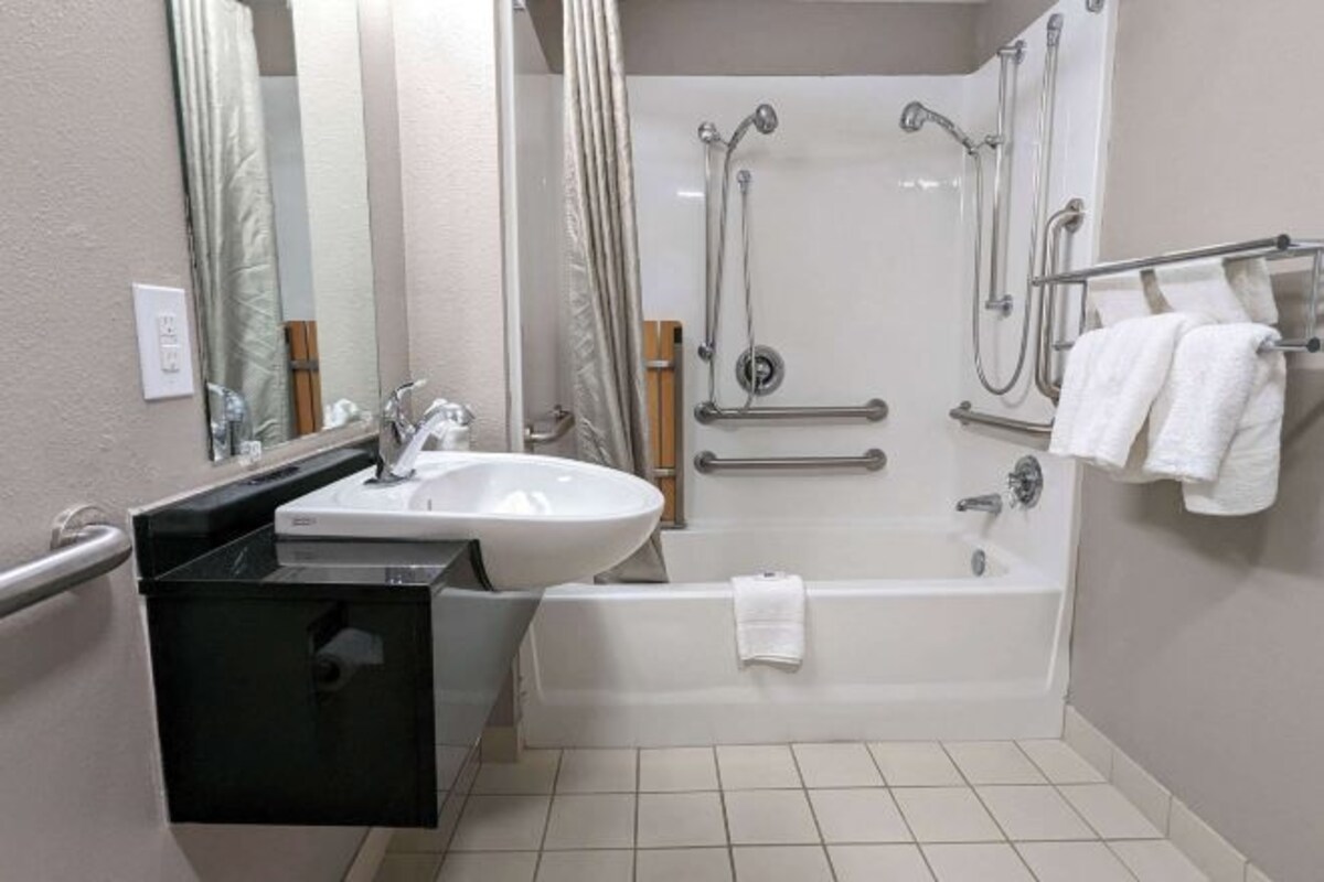 A modern bathroom with a white sink, black countertop, and a walk-in shower with grab bars.