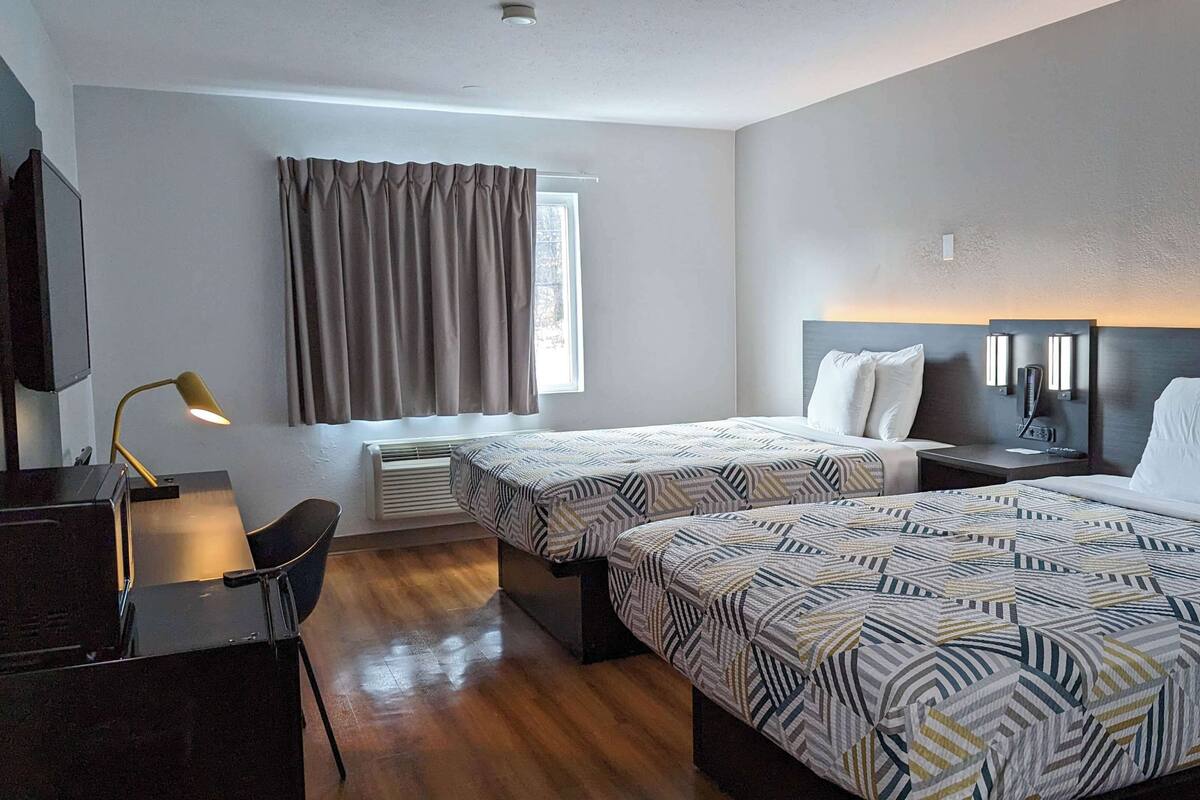 A hotel room with two beds, a desk, a chair, a desk lamp, and a window with curtains.
