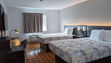 Habitación de hotel con dos camas, un escritorio, una silla, una lámpara de escritorio y una ventana con cortinas.