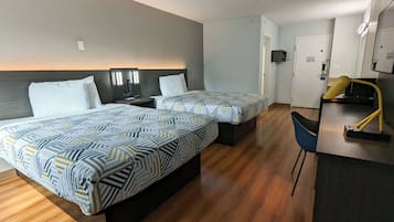 A hotel room with two beds, a desk with a chair, and a door leading to a bathroom.
