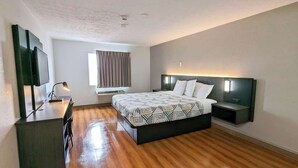 Een moderne hotelkamer met een houten vloer, een groot bed met beddengoed met een patroon, een bureau met een stoel, een flatscreen televisie en een raam met gordijnen.