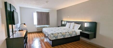 Une chambre d’hôtel moderne avec un plancher en bois, un grand lit avec une literie à motifs, un bureau avec une chaise, un téléviseur à écran plat et une fenêtre avec des rideaux.