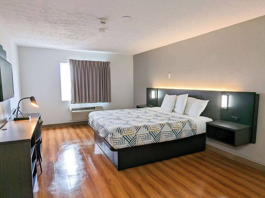 Een moderne hotelkamer met een houten vloer, een groot bed met beddengoed met een patroon, een bureau met een stoel, een flatscreen televisie en een raam met gordijnen.
