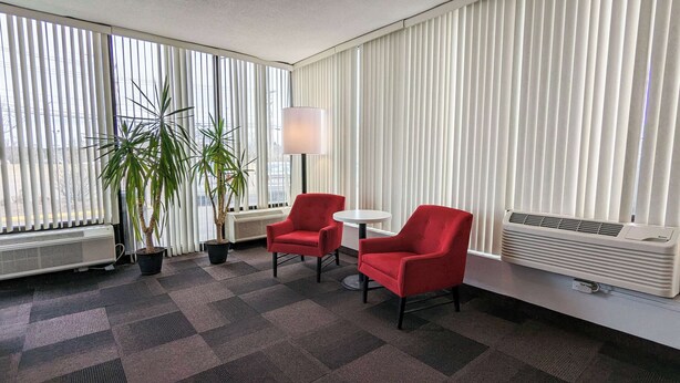 Een hotelkamer met twee rode fauteuils, een klein rond tafeltje, een vloerlamp en twee potplanten.