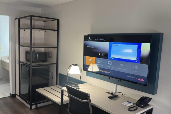 A hotel room with a desk, a TV mounted on the wall, a mini-fridge, a lamp, and a phone on the desk. - La Quinta Inn by Wyndham Auburn Worcester (Auburn)
