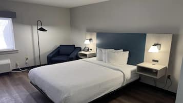 Quarto de hotel com cama, mesas de cabeceira, uma cadeira, escrivaninha, luminária e janela.