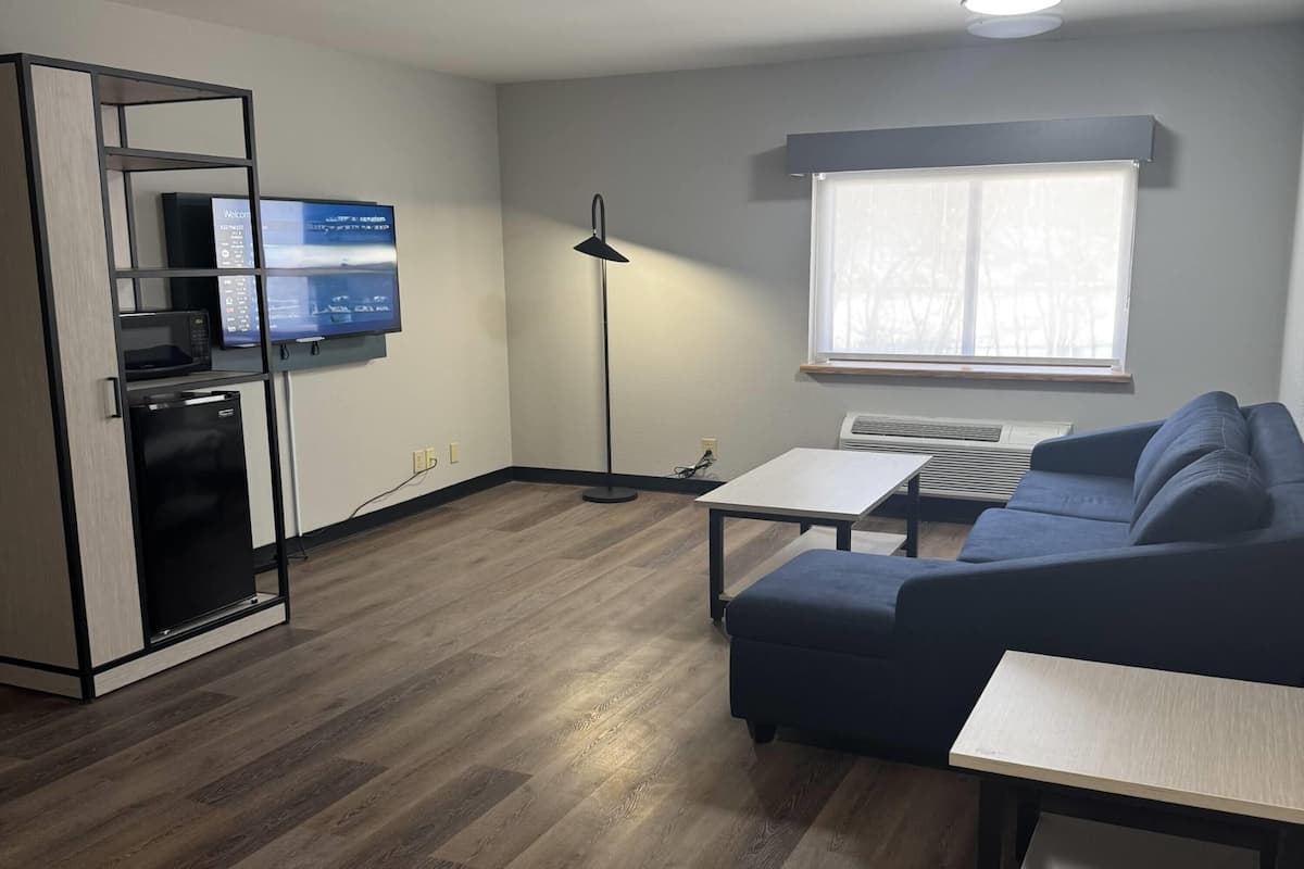 Una sala moderna con un sofá, una mesa de centro, un televisor montado en la pared, una lámpara de pie y una cocina integrada.