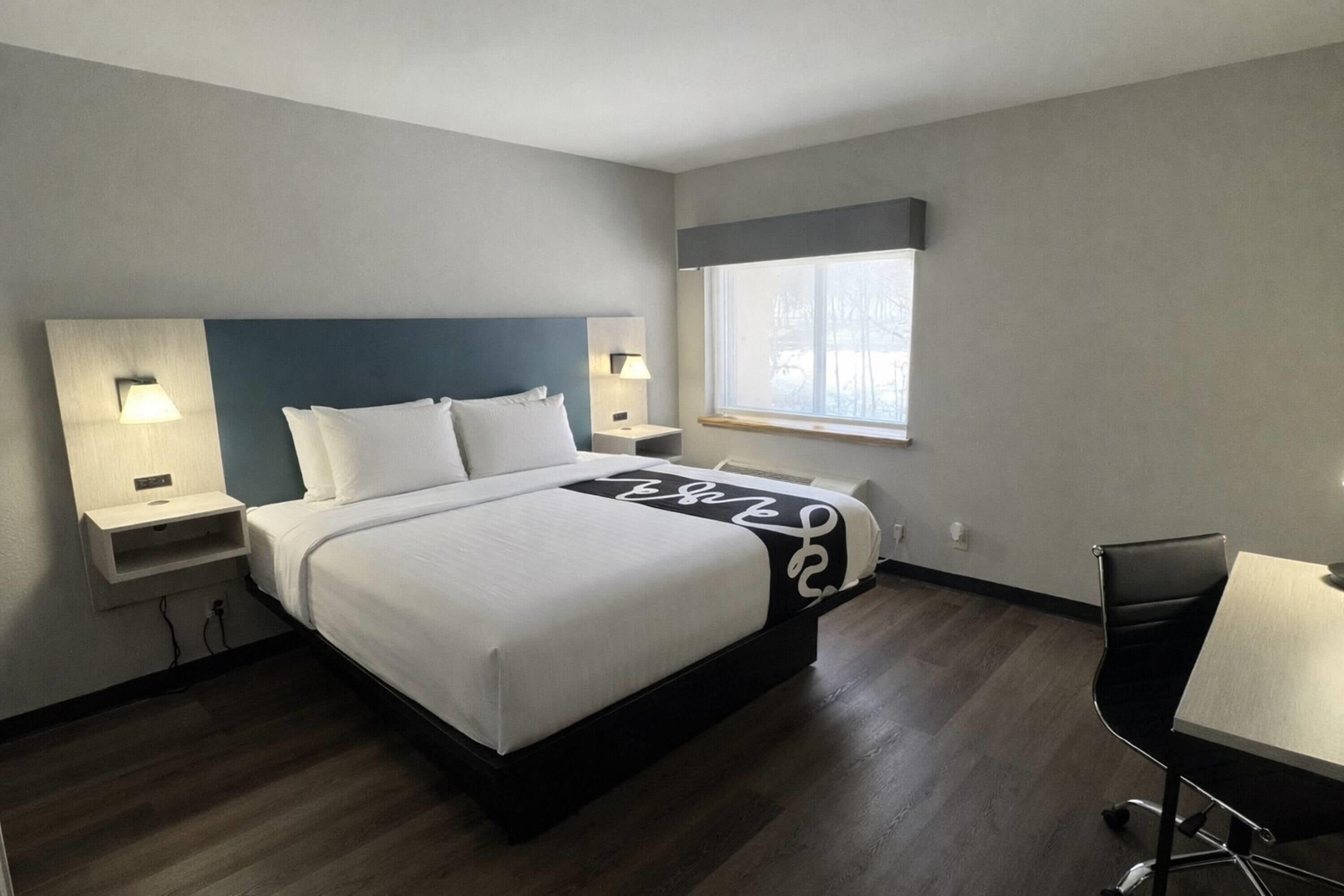 Ein Hotelzimmer mit Bett, Nachttischen mit Lampen, einem Fenster, einem Schreibtisch und einem Stuhl.