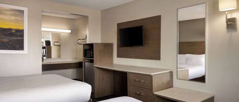 A hotel room with two beds, a desk, a flat-screen TV, a mirror, and a wall-mounted lamp.