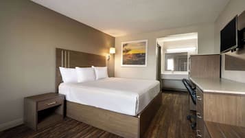 Habitación de hotel con cama, escritorio, silla, televisor y un cuadro en la pared.