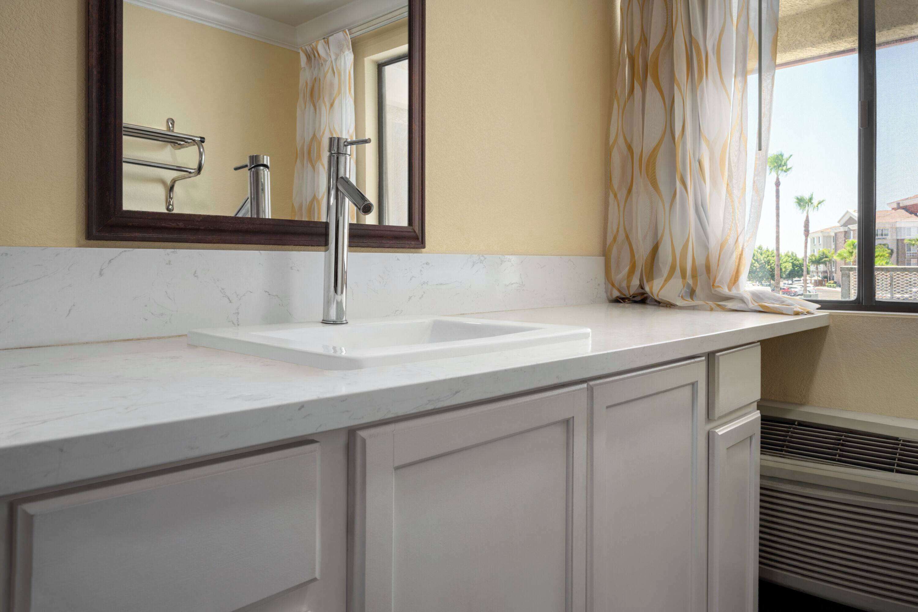 A bathroom with a white sink, a mirror, and a window with curtains.