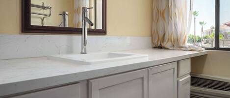 A bathroom with a white sink, a mirror, and a window with curtains.
