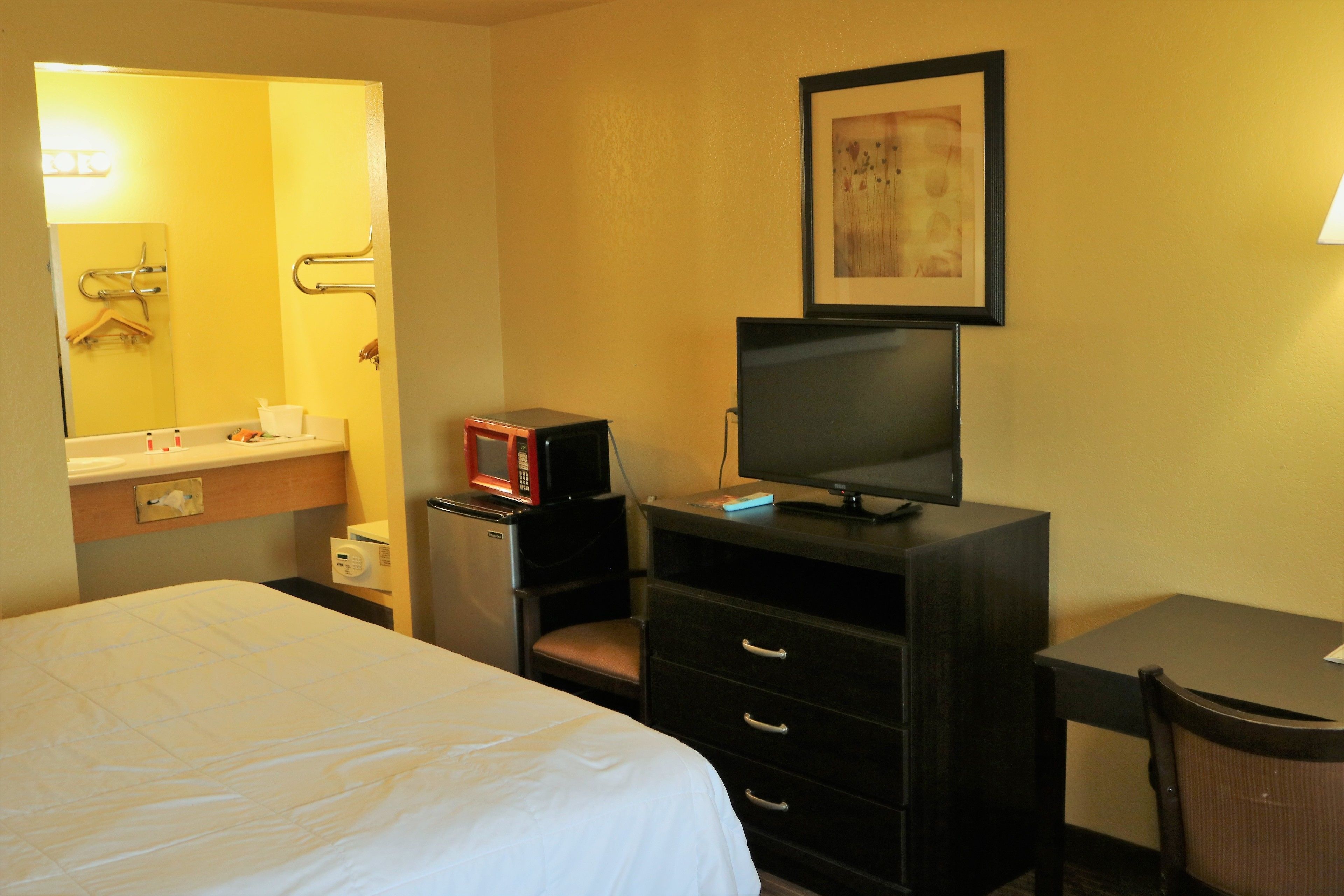Une chambre d’hôtel comprenant un lit, un bureau avec une télévision, une chaise, une commode, un four à micro-ondes et un miroir.