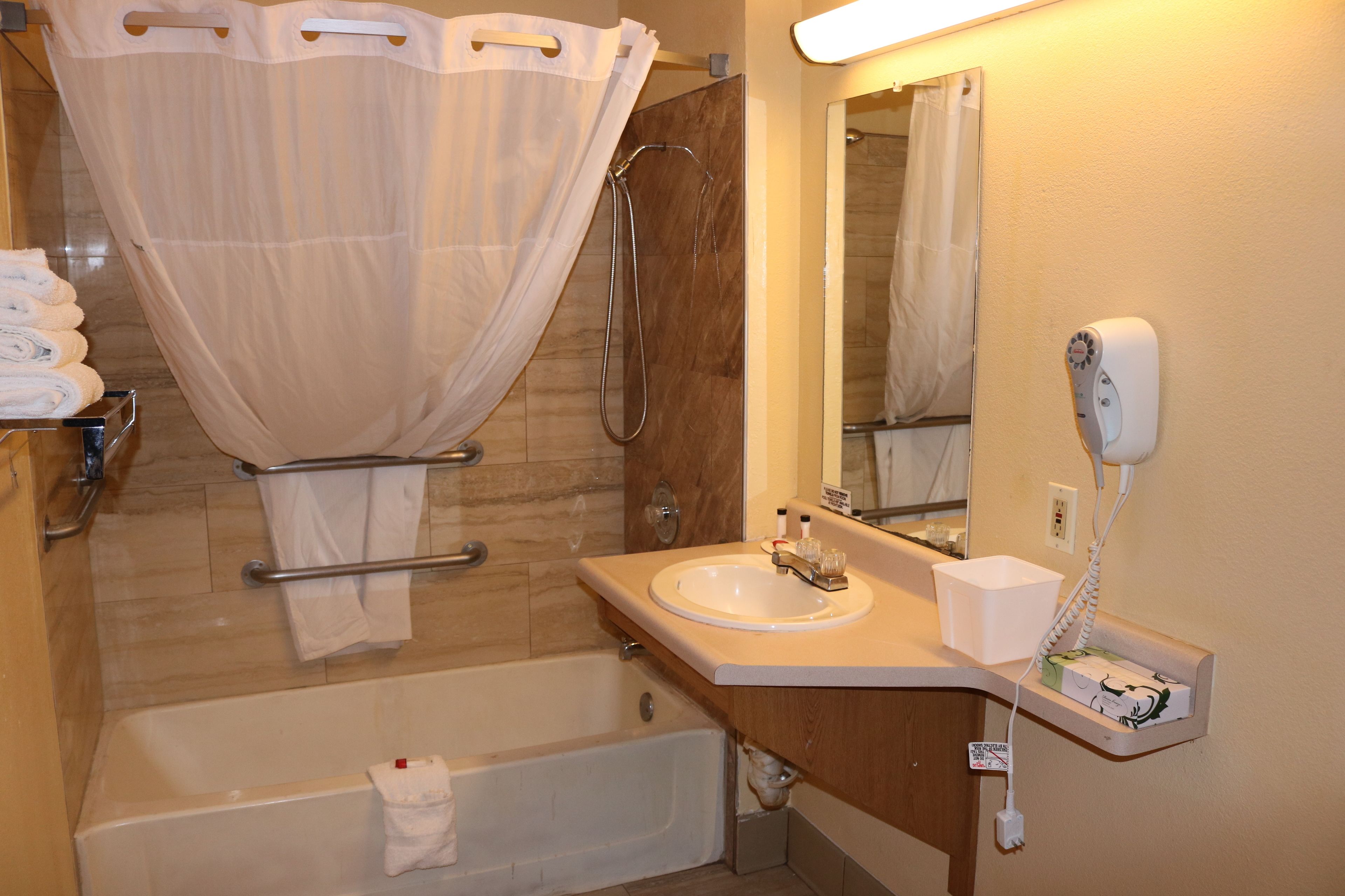A bathroom with a bathtub, a shower, a sink, a mirror, and a hairdryer on the wall.