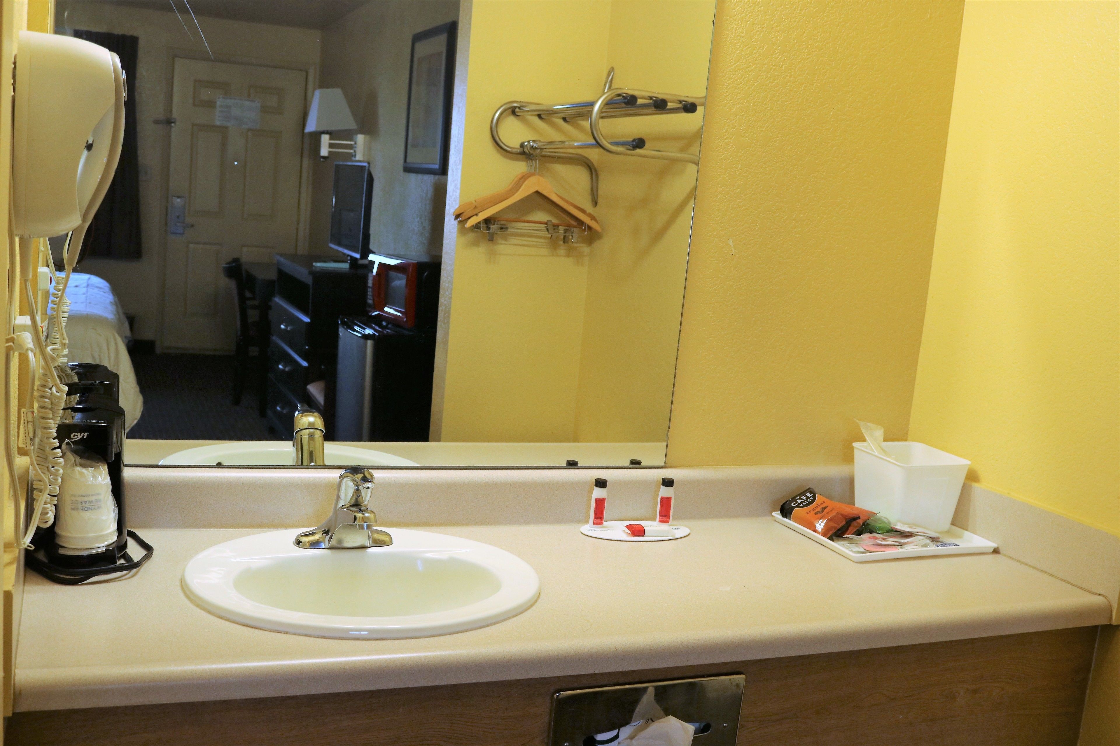 A hotel bathroom with a sink, mirror, and toiletries.