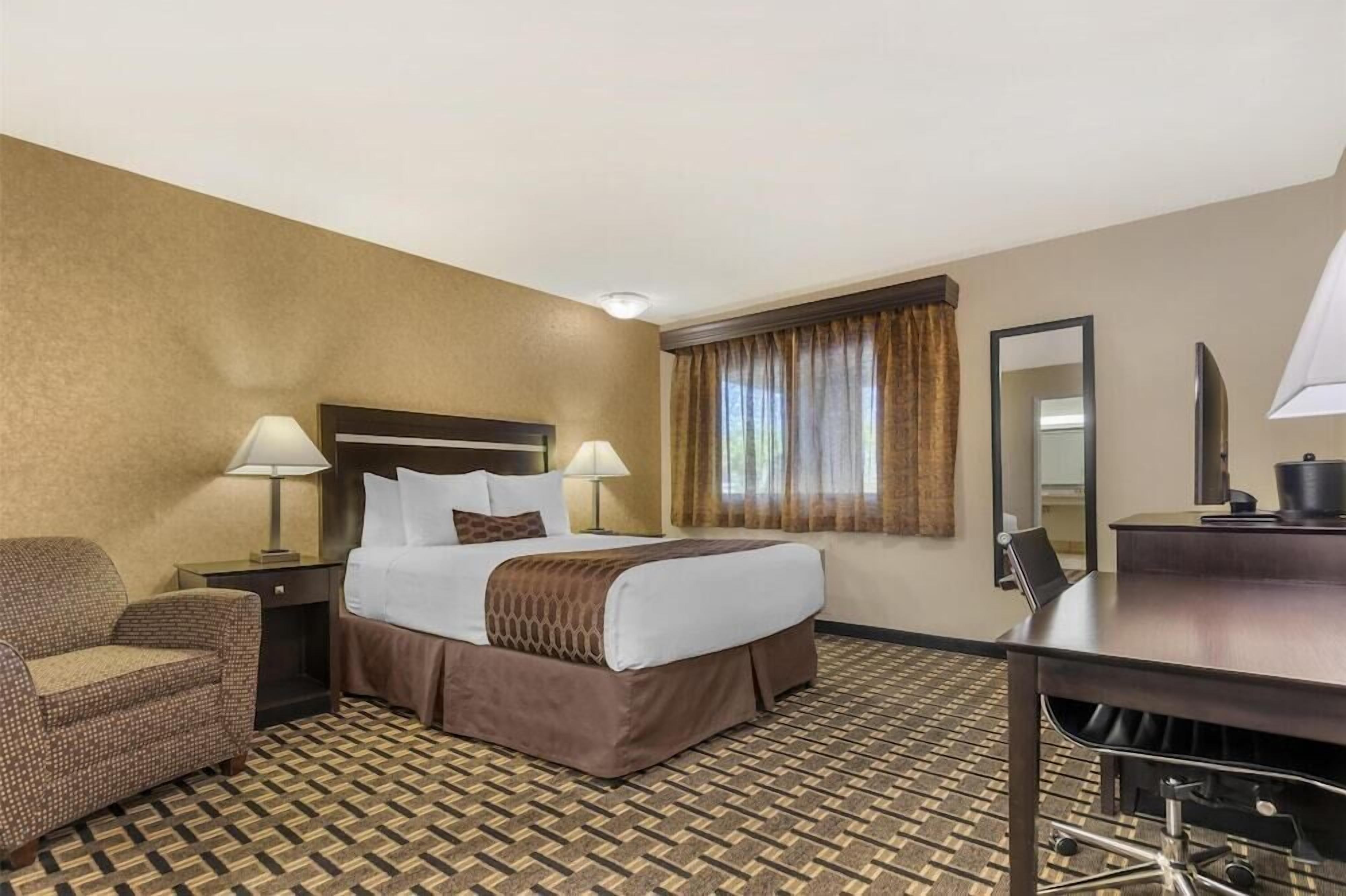 A hotel room with a bed, two bedside lamps, a chair, a desk, and a mirror.