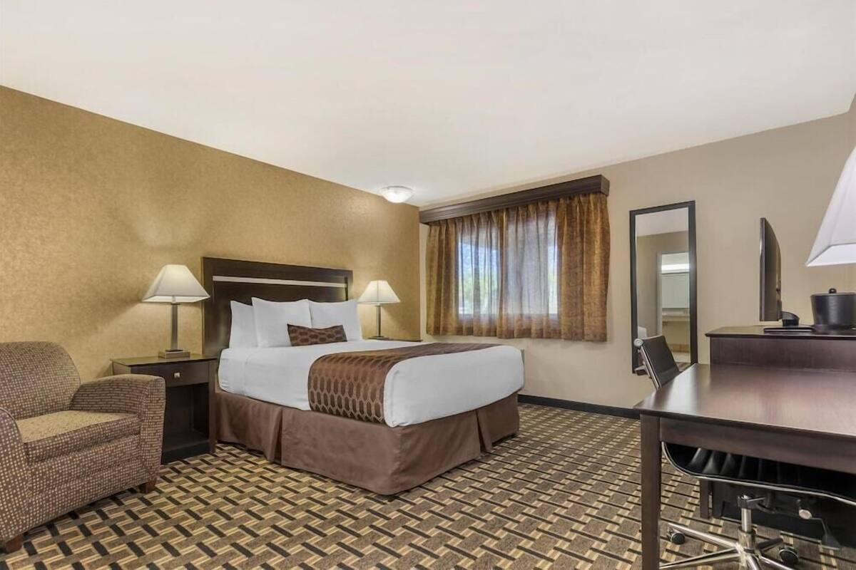 A hotel room with a bed, two bedside lamps, a chair, a desk, and a mirror.