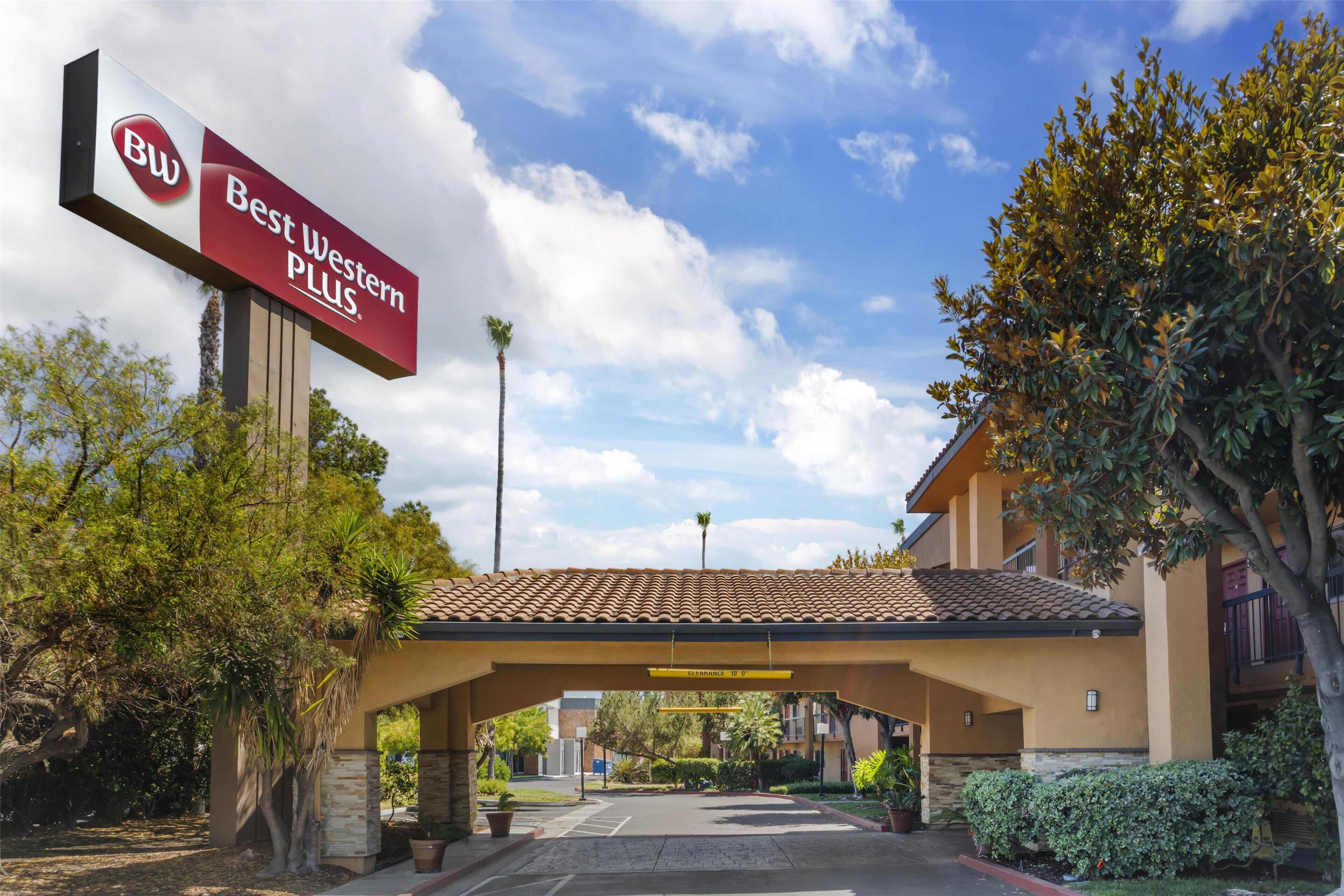 Entrada de un hotel Best Western Plus con estacionamiento techado, palmeras y cielo despejado.