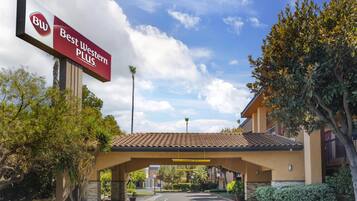 Entrada de un hotel Best Western Plus con estacionamiento techado, palmeras y cielo despejado.