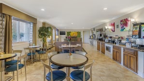 A spacious dining area with round tables and blue chairs, a kitchen area with a coffee machine, and a large window with curtains. - Best Western Plus Pleasanton Inn (Pleasanton)