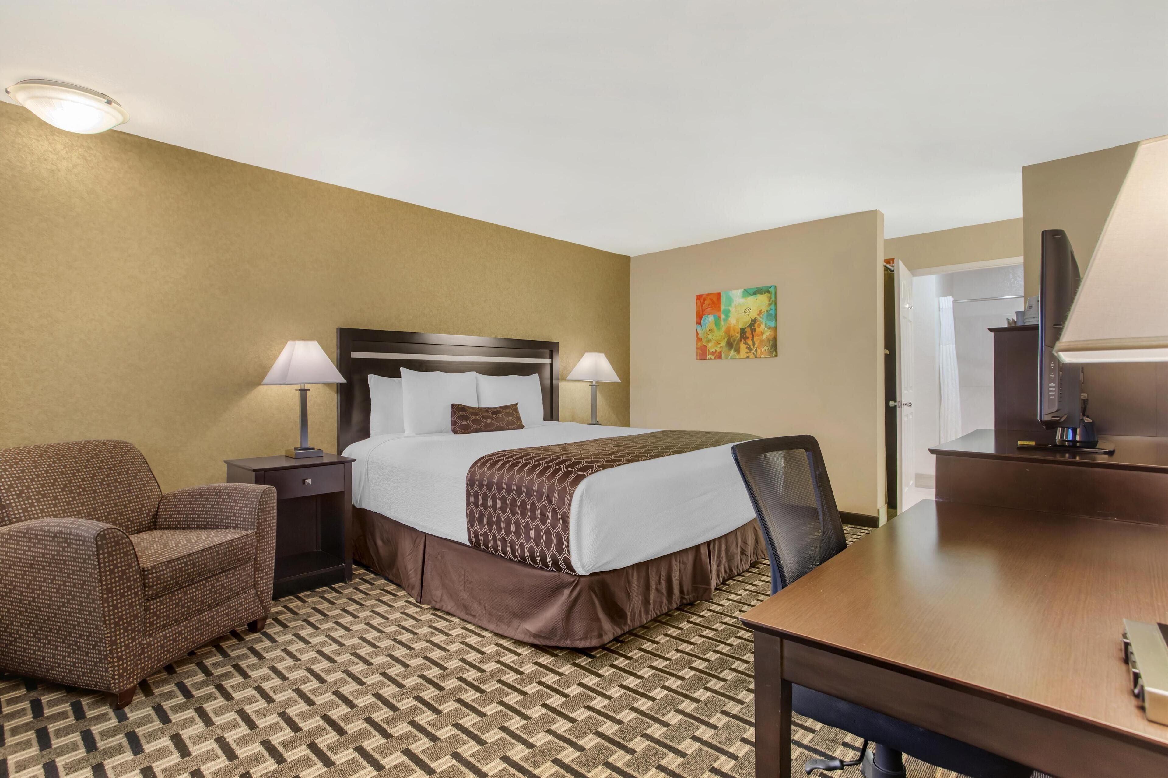Ein Hotelzimmer mit einem Bett, zwei Nachttischlampen, einem Sessel, einem Schreibtisch und einem Fernseher.