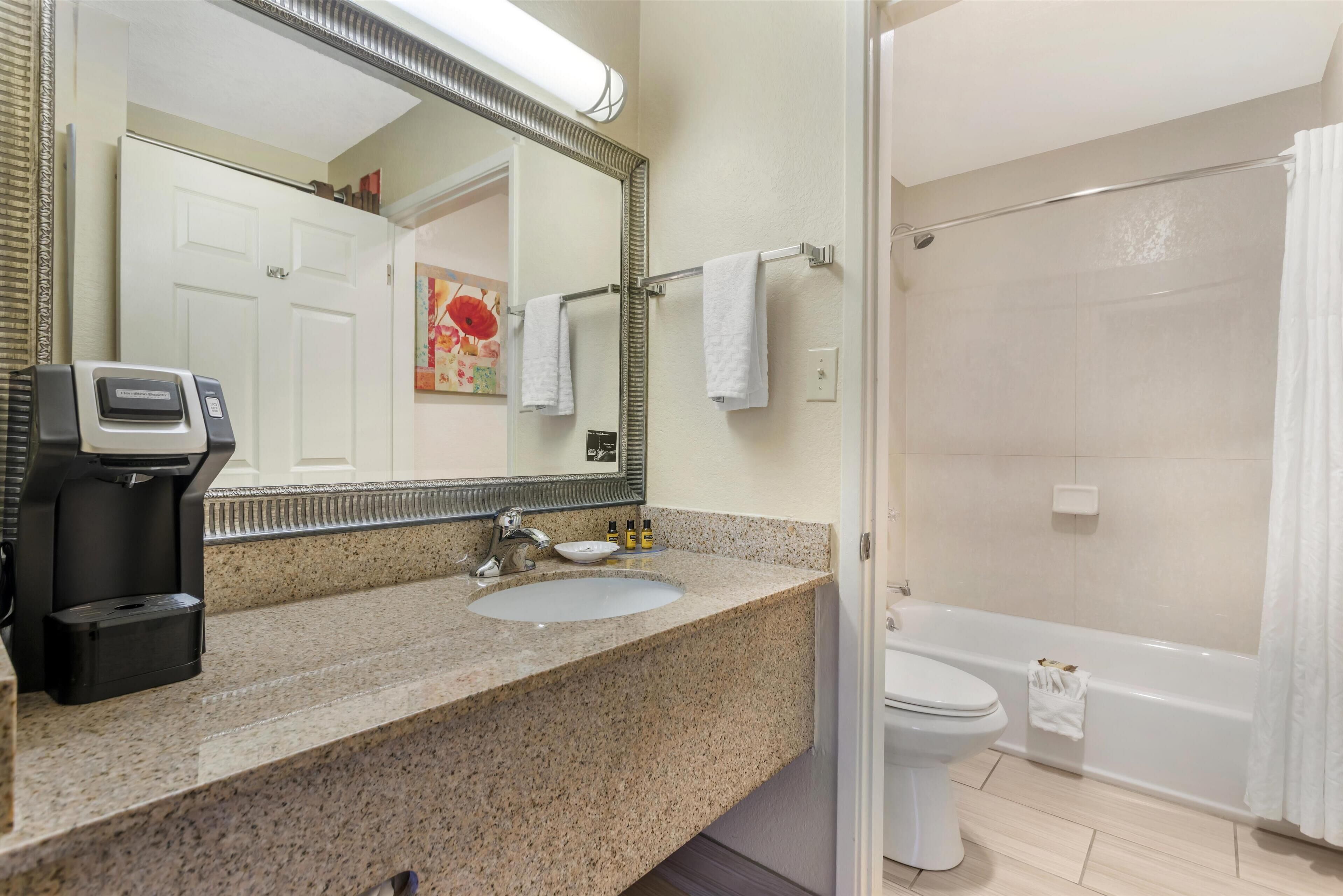 Ein Badezimmer mit Granitwaschtisch, Waschbecken, Toilette und Duschbereich.