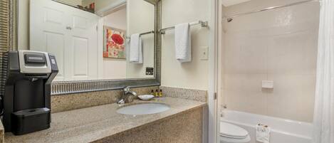 A bathroom with a granite countertop, a sink, a toilet, and a shower area.