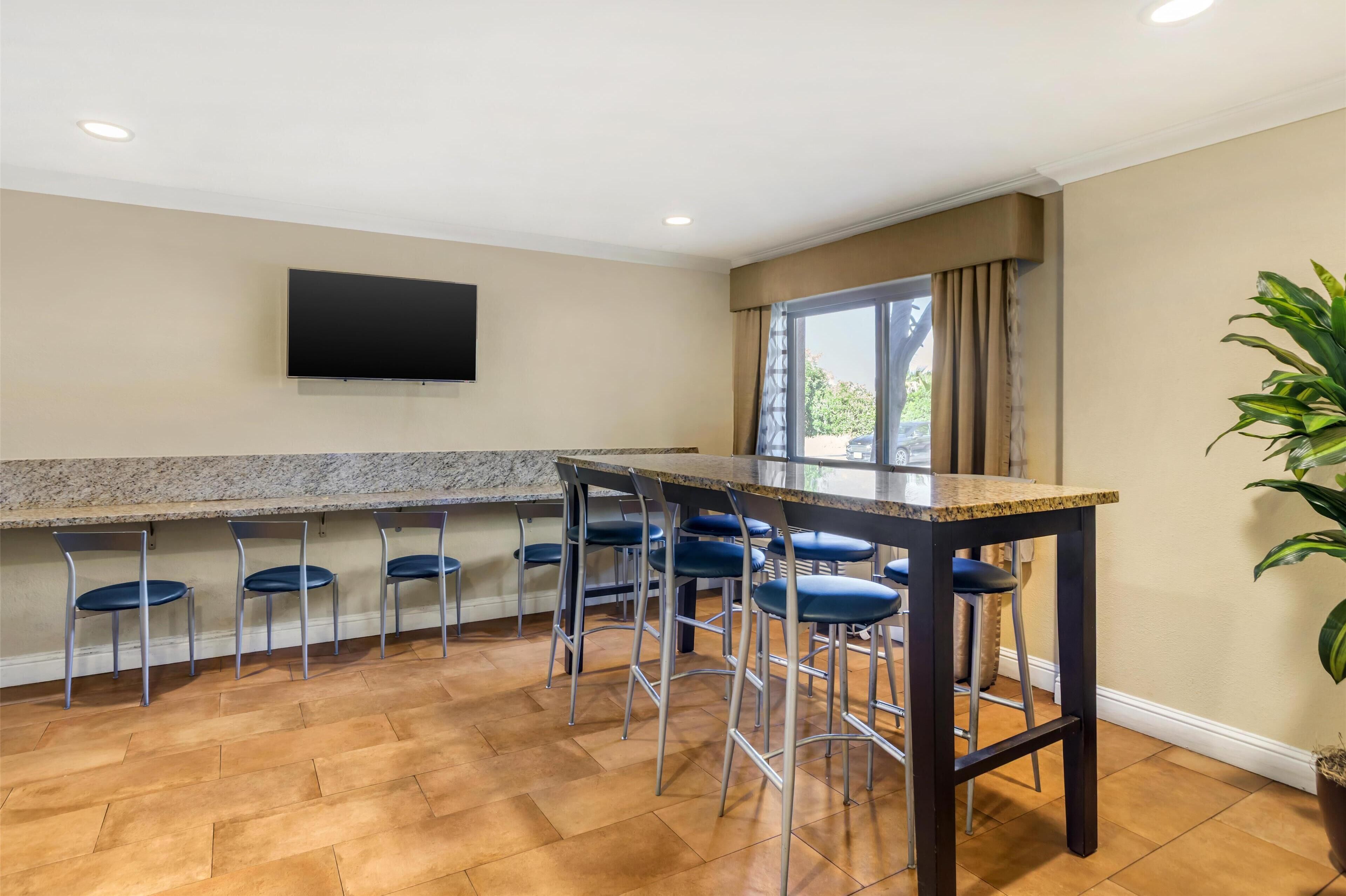 A kitchen with a granite countertop, bar stools, and a flat-screen TV mounted on the wall.